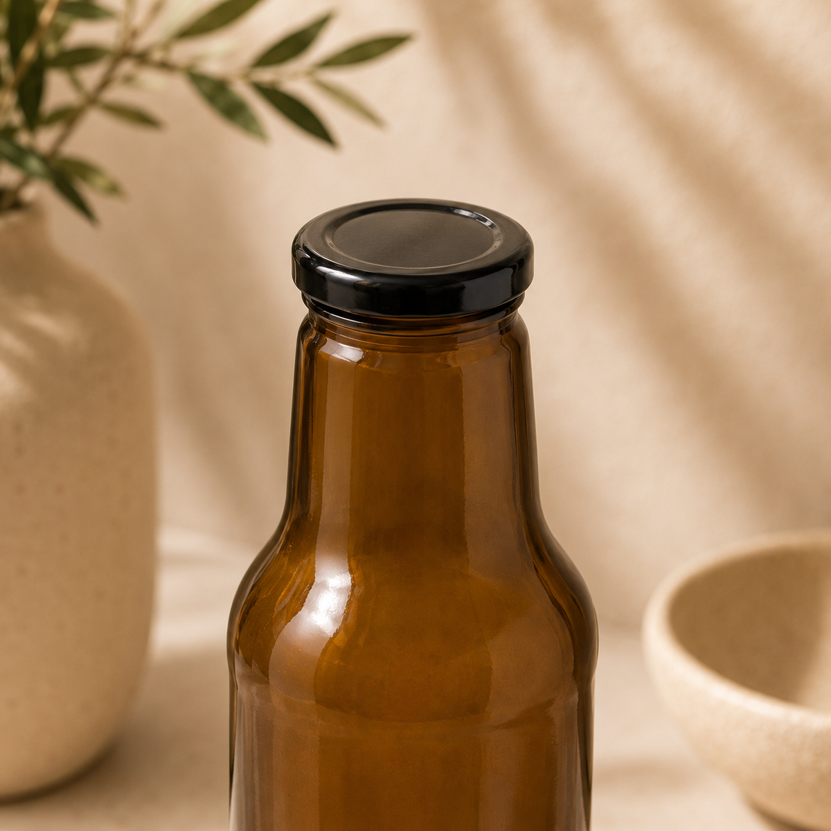 Braune Weithalsflasche mit schwarzem Twist-Off-Verschluss in einer warmen, beigen Produktkulisse.